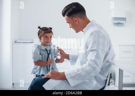 Insegna alla ragazza come usare stetoscopio. Il pediatra giovane lavora con la piccola visitatrice femminile nella clinica Foto Stock