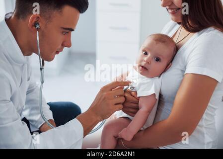 Con l'aiuto della madre. Il pediatra giovane è con il bambino piccolo nella clinica di giorno Foto Stock