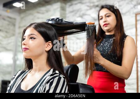 Un parrucchiere fornisce servizi di styling dei capelli ad una giovane donna indiana graziosa, bella donna ottiene i suoi capelli fatti ad un salone, fuoco selettivo. Foto Stock