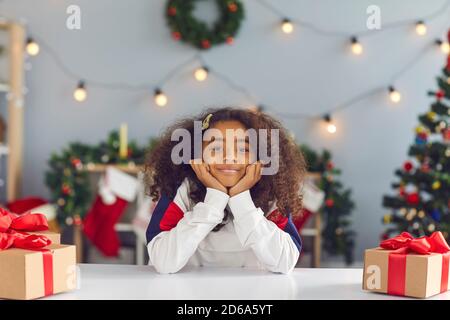 Ragazza felice seduto al tavolo con regali durante la videochiamata O durante la registrazione del vlog di Natale Foto Stock