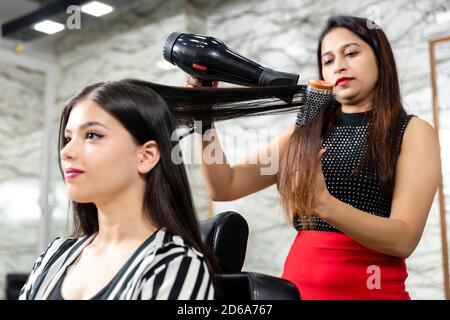 Un parrucchiere fornisce servizi di styling dei capelli ad una giovane donna indiana graziosa, bella donna ottiene i suoi capelli fatti ad un salone, fuoco selettivo. Foto Stock