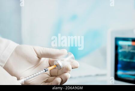 Siringa nella mano del medico, (fuoco sulla cannula arancione dell'ago) sfondo della sala operatoria dell'ospedale. Foto Stock