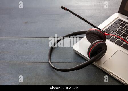 Assistenza clienti, help desk, comunicazione. Concetto di call center e home Office. Cuffia e computer portatile su scrivania in legno blu, vista in primo piano, copia sp Foto Stock