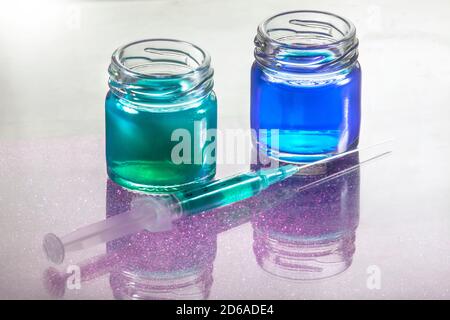 Primo piano Foto di contenitori in vetro liquido blu e verde con Siringa davanti a loro con ombra di grano viola Foto Stock