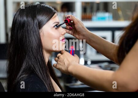 Un giovane modello indiano ad un salone di bellezza, l'artista di trucco che applica eyeliner sul cliente, trucco e concetto di salone di bellezza. Foto Stock