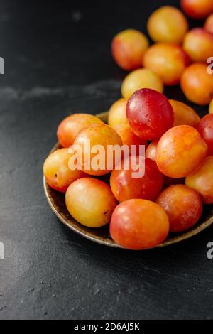 Belle prugne selvatiche mature su piastra di ceramica su sfondo nero Foto Stock