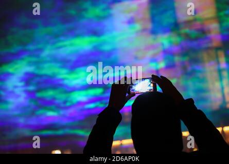 Halle, Germania. 15 Ott 2020. 15 ottobre 2020, Sassonia-Anhalt, Halle (Saale): Un passante scatta foto di aurore generate artificialmente sull'Hallmarkt utilizzando raggi laser e nebbia. L'installazione leggera "Borealis" dell'artista svizzero Dan Archer fa parte del Silver Salt Science and Media Festival di quest'anno. Sotto il motto 'Home Earth' si svolgerà dal 14 al 18 ottobre a Halle (Saale). Foto: Jan Woitas/dpa-Zentralbild/dpa Credit: dpa Picture Alliance/Alamy Live News Foto Stock
