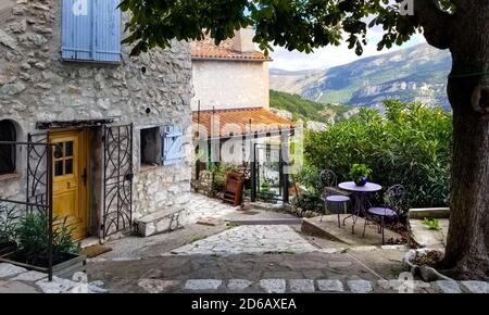 Un piccolo patio ombreggiato all'esterno di un antico edificio in pietra nel villaggio murato di Gourdon, in Francia, nella regione Provenza-Costa d'Azure. Foto Stock