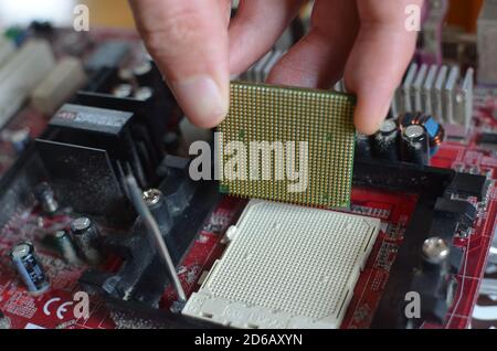 Una mano che rimuove una CPU (chip del processore) dalla scheda madre di un vecchio computer. Foto Stock