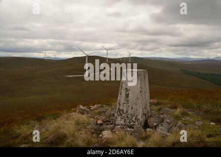 Il trig del Ordnance Survey punta sulla cima della collina Meall A' Gruidididh con un windfarm alle spalle, vicino a Lairg, Highlands scozzesi, Regno Unito. Foto Stock