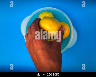 Vista dall'alto della mano che raccoglie una mela gialla da a. contenitore su sfondo blu Foto Stock