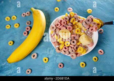 Colazione sana con cereali e banana. Dall'alto della ciotola con deliziosa e sana colazione fatta con colorati anelli di cereali e banana con latte Foto Stock