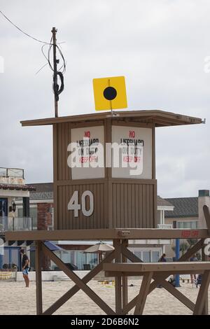 Una Lifeguard che batte una bandiera di blackball che dice ai surfisti di lasciare l'acqua e consentire solo ai nuotatori. Torre 40 a Newport Beach, California, Stati Uniti Foto Stock