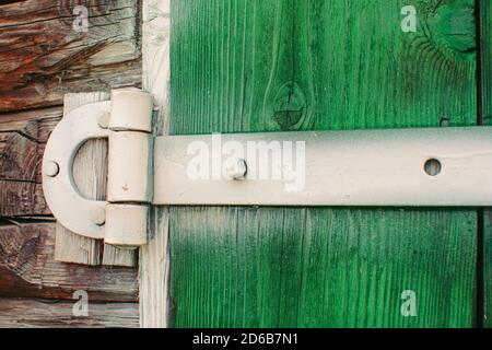 Cerniere dipinte in ferro bianco su cancelli di legno verde di capannone da vicino. Sfondo dettagliato testurizzato con tavole di legno di fienile è dipinto di vivace dolore verde Foto Stock