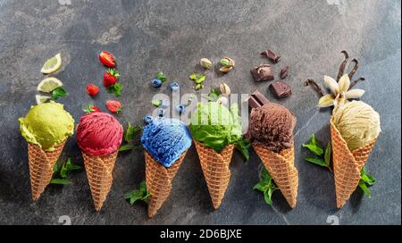 Set di vari gelati colorati in coni di cialde con fette di frutta su sfondo grigio. Vista del layout. Foto Stock