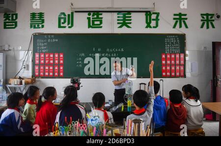 (201016) -- LUXI, 16 ottobre 2020 (Xinhua) -- li Xuezhan (posteriore) dà una lezione di scienza a scuola nella contea di Luxi, nella provincia di Jiangxi della Cina orientale, 14 ottobre 2020. Ogni volta che li Xuezhan entra nella scuola centrale nella città di Xuanfeng della contea di Luxi con la sua valigia piena di sussidi didattici fatti a mano, sarà seguito e circondato da studenti. Li, 58 anni, divenne insegnante di scienze nel 1996. A causa della mancanza di ausili didattici, ha dovuto raccogliere bottiglie vuote, legno, pneumatici rotti e trasformarli in ausili didattici per la classe scientifica. Ora che le condizioni di insegnamento della scuola sono migliorate, li e il suo Foto Stock