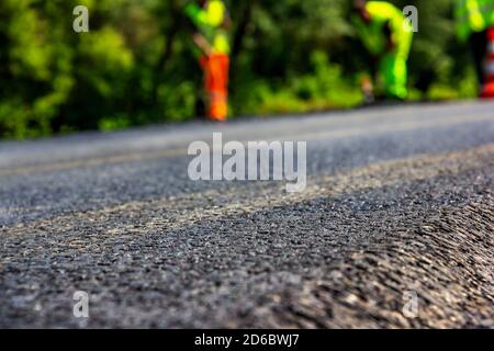 Primo piano di una nuova strada recentemente asfaltata con i costruttori in uniforme sul retro fon Foto Stock