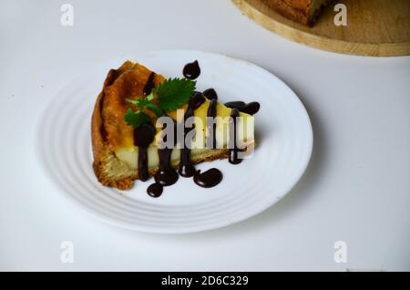fetta di cheesecake decorata con foglie di menta e salsa al cioccolato isolata su sfondo bianco Foto Stock
