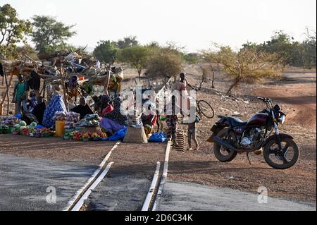 BURKINA FASO, Kaya, linea ferroviaria abbandonata per le miniere di minerale di manganese a Tambao, costruito durante il tempo di Thomas Sankara, persone che vendono ortaggi al passaggio ferroviario stradale / BURKINA FASO, Kaya, von Sankara gebaute Eisenbahnzu Linie den Mangan Lagerstätten a Tambao, Eisenbahnstrecke schon seit Jahren ausser Betrieb, Menschen verkaufen Gemüse und Obst an einem Bahnübergang Foto Stock