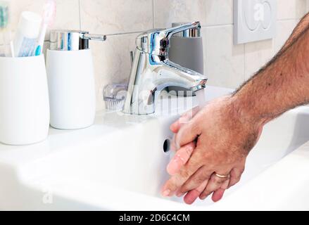 un uomo che si lava le mani in un lavello di ceramica bianca. Cura personale e pulizia. Rubinetto cromato e contenitore per sapone Foto Stock