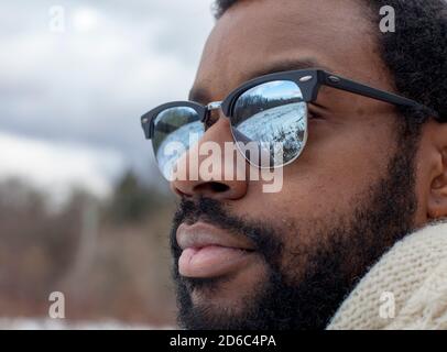 Un uomo che indossa occhiali da sole in stile Clubmaster si affaccia su una palude ghiacciata, riflessa nelle lenti dei suoi occhiali, in una giornata invernale a Ithaca, NY Foto Stock