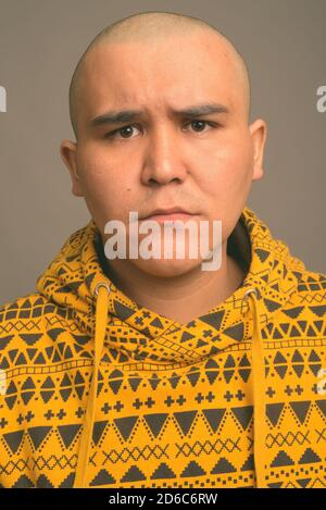 Giovani bald uomo asiatico contro uno sfondo grigio Foto Stock