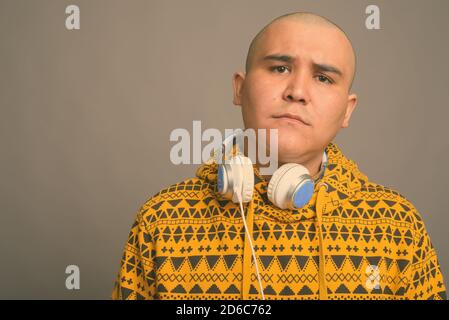 Giovani bald uomo asiatico che indossano le cuffie contro uno sfondo grigio Foto Stock