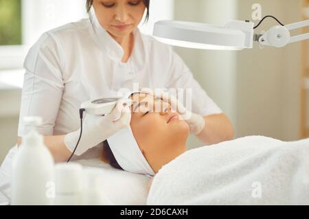 Donna dermatologa che fa l'apparecchiatura di ultrasuoni pulizia del viso con macchina speciale per la giovane donna Foto Stock