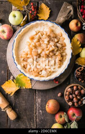 Sfondo da forno con torta di mele classica cruda, ingredienti da forno e utensili. Torta fatta in casa circondata da frutta fresca Foto Stock