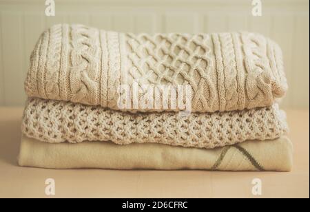 Su uno sfondo beige chiaro, tre morbidi pullover in lana con diversi motivi sono impilati in un palo pulito. Il comfort di casa. Abiti caldi per Foto Stock