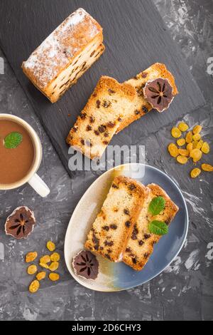 Torta fatta in casa con uvetta, persimmon secco e una tazza di cioccolata calda su fondo nero in cemento. Vista dall'alto, posa piatta, spazio copia. Foto Stock