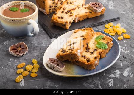 Torta fatta in casa con uvetta, persimmon secco e una tazza di cioccolata calda su fondo nero di cemento. Vista laterale, primo piano, spazio di copia. Foto Stock