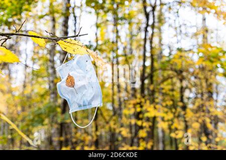 maschera monouso sporca appesa al ramo dell'albero con il giallo partenza nel parco cittadino il giorno d'autunno Foto Stock