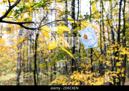 maschera sanitaria usata appesa al ramo dell'albero con il giallo partenza nel parco cittadino il giorno d'autunno Foto Stock