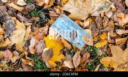 vista panoramica della maschera usata sporca in caso di caduta bagnata foglie sul prato nel parco cittadino in autunno Foto Stock