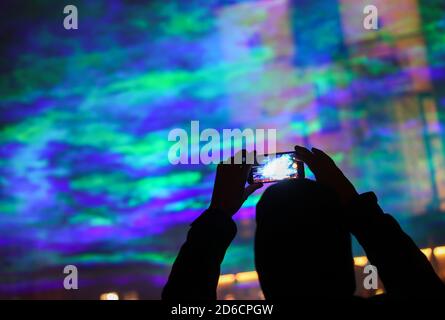 15 ottobre 2020, Sassonia-Anhalt, Halle (Saale): Un passante scatta foto di aurore generate artificialmente sull'Hallmarkt utilizzando raggi laser e nebbia. L'installazione leggera "Borealis" dell'artista svizzero Dan Acher fa parte del Silver Salt Science and Media Festival di quest'anno. Sotto il motto 'Home Earth' si svolgerà dal 14 al 18 ottobre a Halle (Saale). Foto: Jan Woitas/dpa-Zentralbild/dpa Foto Stock