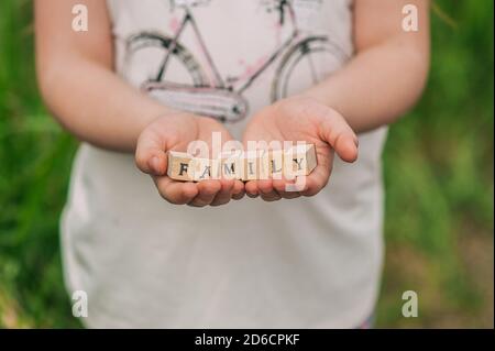 Mani di un bambino adolescente che tiene i cubi di legno con le lettere che compongono la famiglia di iscrizione. Foto Stock