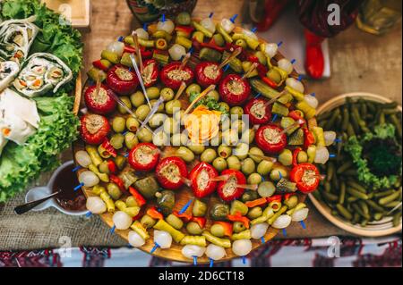 Tavola di legno con diverse fette di cetriolo, cipolla, olive e peperoni ripieni su spiedini. Foto Stock