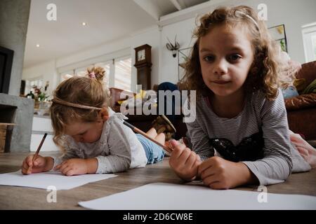 Due bambini piccoli che si trovano sul pavimento di legno perchè colorarsi dentro come madre e padre si siedono sul divano comodo nel soggiorno. Foto Stock