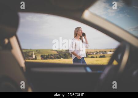 Donna piuttosto anziana al volante della sua auto, con una pausa durante un lungo viaggio, facendo una telefonata Foto Stock