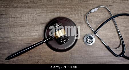 Gavel del giudice accanto stetoscopio medico su tavola di legno. Immagine panoramica. Foto Stock