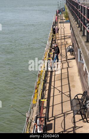 Pescatori alla fine di Southend Pier, Southend on Sea, Essex, Regno Unito. Canne multiple sulle ringhiere di pesca nel Tamigi estuario. Pesca in mare. Acqua salata Foto Stock