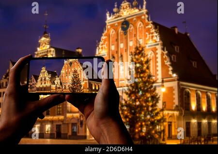 Turista che scatta la foto dell'albero di Natale a riga. Casa dei Blackheads con albero di Natale di notte, città vecchia riga, Lettonia Foto Stock