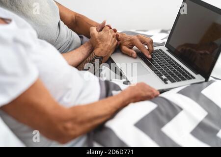 Coppia senior che utilizza un computer portatile a letto - persone mature divertirsi con il computer portatile mentre si sdraia sotto le coperte in camera da letto Foto Stock
