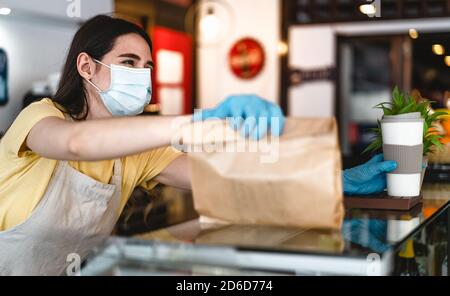 Il proprietario del bar lavora solo con gli ordini di take away durante l'epidemia di virus corona - giovane donna operatrice che indossa la maschera chirurgica del viso che dà pasto da asporto Foto Stock