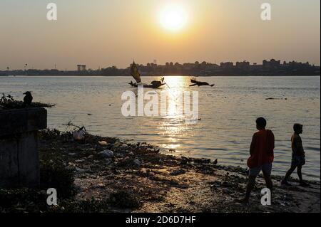 22.02.2011, Kolkata, Bengala Occidentale, India - il profilo della gente sulle rive del fiume Hugli durante un tramonto con la stazione di Howrah in lontananza. Foto Stock