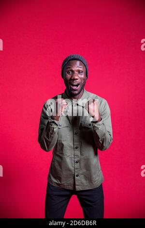 Giovane uomo nero con bocca aperta in eccitazione guardando la macchina fotografica. Isolato. Verticale. Scatto medio. Foto Stock