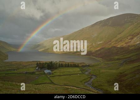 Arcobaleno vivido attraverso il bacino idrico di Talla in autunno, Scottish Borders.nuvoloso Foto Stock