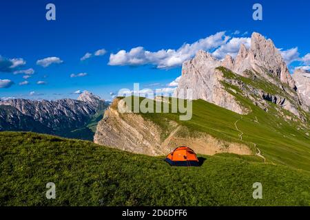 Una tenda arancione sui pascoli di montagna che circondano le scogliere ripide e ruvide e le cime della formazione di montagna Seceda, Secèda, parte del Foto Stock