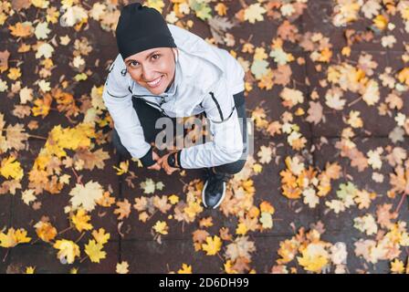 Sorridi sinceramente la donna caucasica che riposa dopo il jogging mattutino siediti sul sentiero del parco della città coperto di acqua partenza autunno giallo Foto Stock
